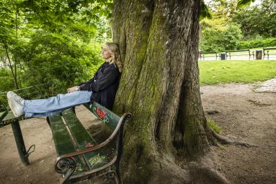 Kelly Young sidder på en alternativ måde på en bænk op ad et træ