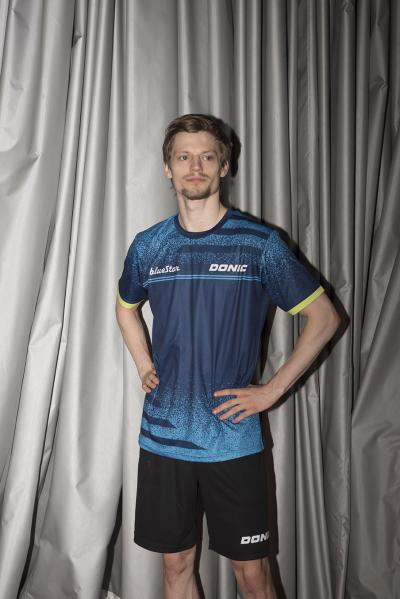 Den danske bordtennisstjerne og OL-helt Anders Lind står foran et baggrundslærred og kigger forbi kameraet