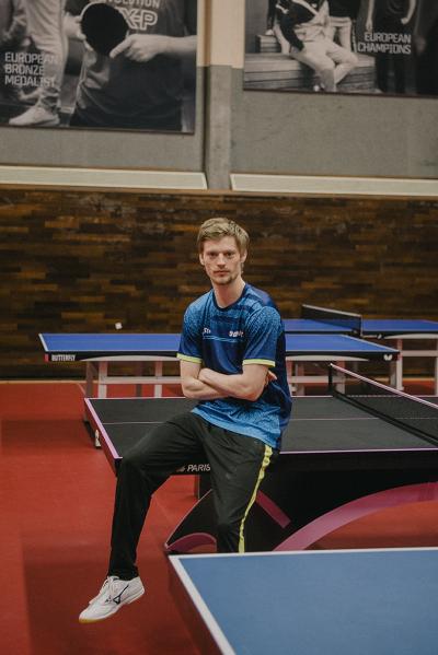 Den danske bordtennisstjerne og OL-helt Anders Lind sidder på kanten af et bordtennisbord og kigger i kameraet