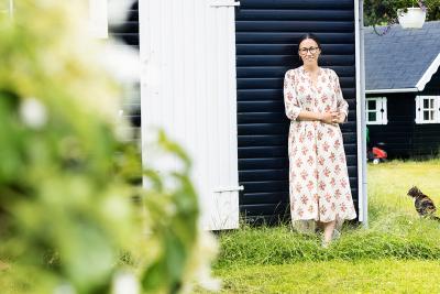 Mette Cornelius læner sig op ad sommerhusmur med en kat i baggrunden