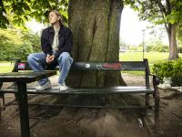 Kelly sidder på en bænkeryg med graffiti