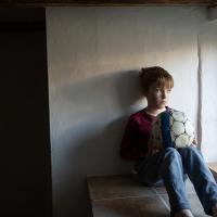 Dreng sidder med bold, kigger ud af vindue